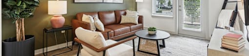A living room with a brown leather couch, a white chair, a small table, a potted plant, and a ceiling fan.