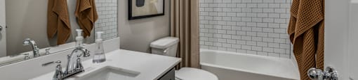 A bathroom with a white sink, toilet, and a shower with a brown towel hanging on the door.