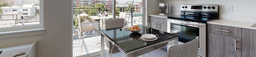 A modern kitchen with a table and chairs in front of a window overlooking a cityscape.