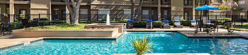 A swimming pool surrounded by trees and a building in the background.