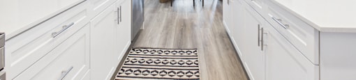 A modern kitchen with white cabinets and a black and white rug on the floor.