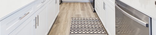 A modern kitchen with white cabinets and a black and white rug on the floor.