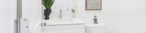 A white bathroom with a toilet, sink, and cabinets.