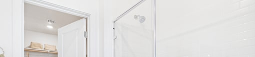 A white bathroom with a walk-in shower and a doorway leading to another room.