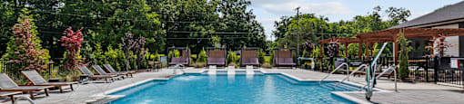 A large swimming pool with a hot tub in the middle surrounded by trees.