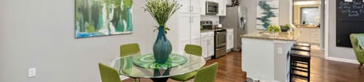 a dining area with a glass table and chairs and a kitchen in the background