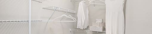 a walk in closet in a bedroom with white walls and a white dress hanging on the wall