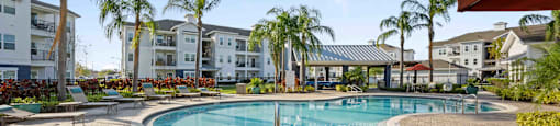 a resort style swimming pool with chaise lounge chairs and palm trees in the background
