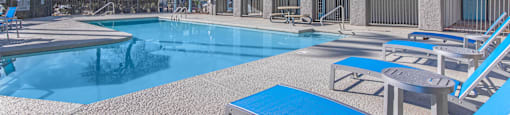 A pool with sun loungers and a building with a red roof.