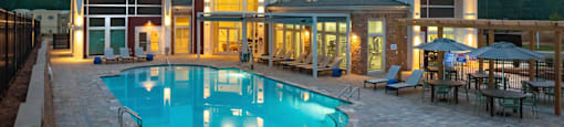 a resort style pool with lounge chairs and umbrellas at dusk