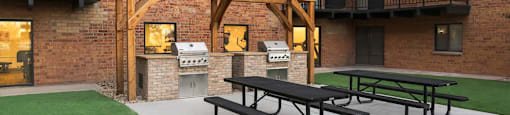A patio with a picnic table and a grill in front of a brick building.