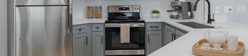 A modern kitchen with a stainless steel refrigerator and a wooden tray with tea cups on the counter.