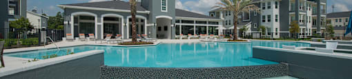 A pool with sun loungers in front of a hotel.