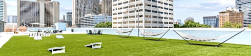 A grassy area with a hammock and benches in the foreground and a city skyline in the background.