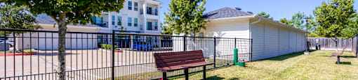 A park with a bench, a tree, and a fence.