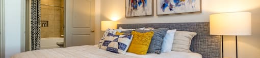 A bedroom with a large bed and two abstract paintings on the wall.
