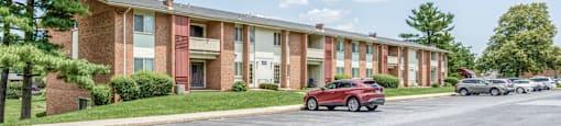 A red car is parked on the street in front of a brick apartment building.