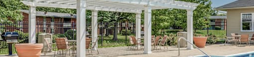A pool area with a white pergola and patio furniture.