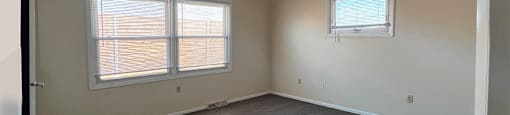 A room with grey carpet and two windows.