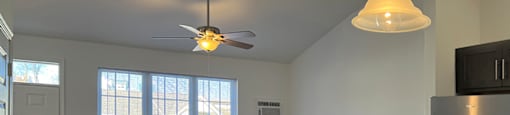 A kitchen with a refrigerator, ceiling fan, and a window.