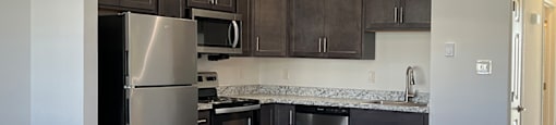 A kitchen with a stainless steel refrigerator and black cabinets.