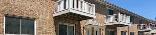A white car is parked in front of a brick building with a balcony.