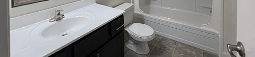 A bathroom with a white sink, black cabinetry, and a walk-in shower.