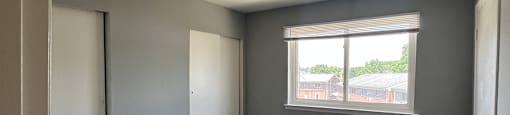 A room with grey carpet and a window overlooking a building.