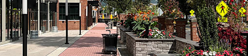 A brick walkway leads to a building with a bench and flowers on the side.