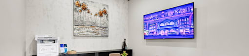 A room with a white table and chairs, a painting on the wall, and a TV screen showing a cityscape.