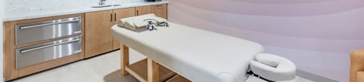 A room with a massage table and a kitchen area.