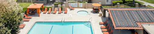 A swimming pool with orange lounge chairs and a building in the background.