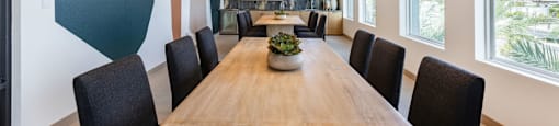A long wooden table is surrounded by black chairs in a room with a large window.