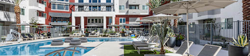 A pool area with sun loungers and a building in the background.