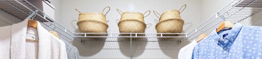 A laundry room with clothes hanging and baskets on the shelf.