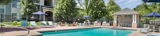 a swimming pool with chairs and umbrellas and a building in the background at Ascent Apartments, Cottonwood Heights, UT