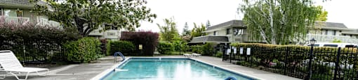 a swimming pool with a fence and trees in the background at OTAVON APARTMENTS, Novato, CA 94947