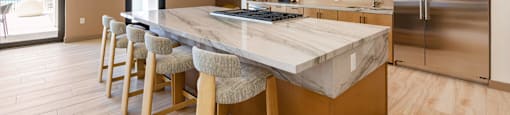 A kitchen with a marble countertop and wooden bar stools.