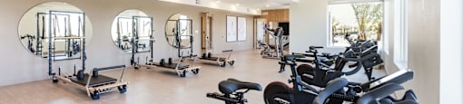 A gym with a row of stationary bikes and mirrors on the wall.