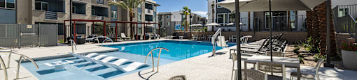 a swimming pool with tables and umbrellas in front of an apartment building at BASE APARTMENT HOMES, LAS VEGAS, Nevada