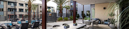 a patio with tables and chairs and palm trees at BASE APARTMENT HOMES, LAS VEGAS, 89166