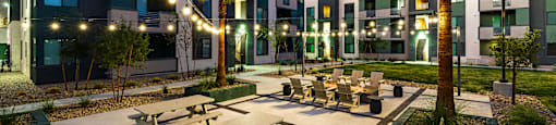 A sunset view of a courtyard with tables and chairs and a palm tree.