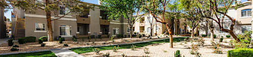 a courtyard with trees and a sidewalk in front of apartment buildings at THE CLUBS AT RHODES RANCH APARTMENT HOMES, Las Vegas, NV, 89148