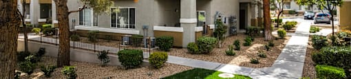 an apartment building with a sidewalk and trees at THE CLUBS AT RHODES RANCH APARTMENT HOMES, Las Vegas, NV
