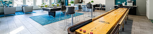A pool table is in the middle of a room with chairs and a bar.