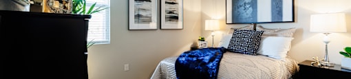 A bedroom with a bed, nightstand, and two framed pictures on the wall.