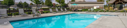 A large outdoor swimming pool surrounded by a fence and trees.