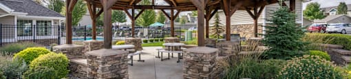 Apartments In Spokane, WA With In-Unit Washer And Dryer - Deer Creek - Pavilion With Timber-Frame Roof Supported By Stone-Clad Pillars, And Picnic Tables With Benches On A Clean Concrete Pad.