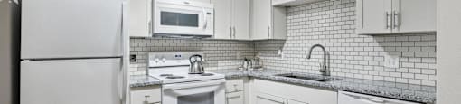 A white kitchen with a refrigerator, microwave, oven, and sink.