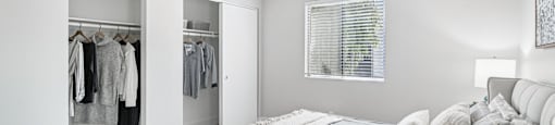 A bedroom with a bed, pillows, and a closet with clothes.